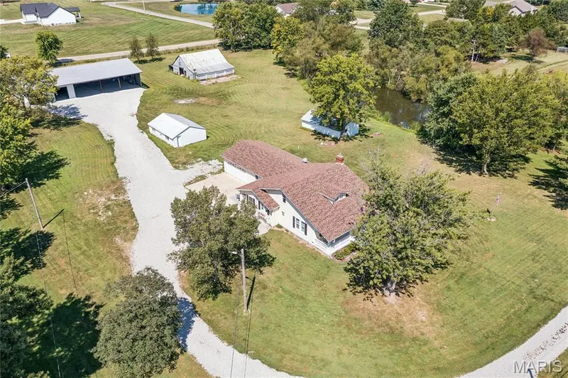 Spacious property featuring a primary residence, a large outbuilding with an open bay, a white storage shed, a rustic barn, and a natural water feature — 435 Highway T, Foristell, MO 63348