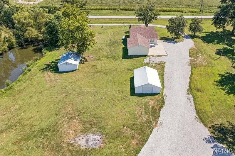 Expansive property featuring a single-story residence, two outbuildings, a gravel driveway, and a natural water feature — 435 Highway T, Foristell, MO 63348