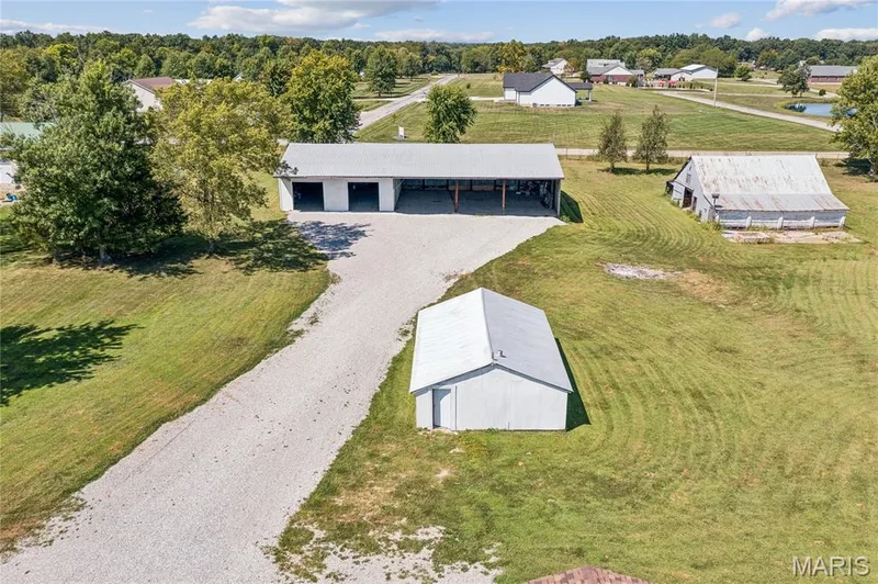 Gravel driveway leading to a multi-bay outbuilding with a covered area, a detached storage building, and an additional barn structure — 435 Highway T, Foristell, MO 63348