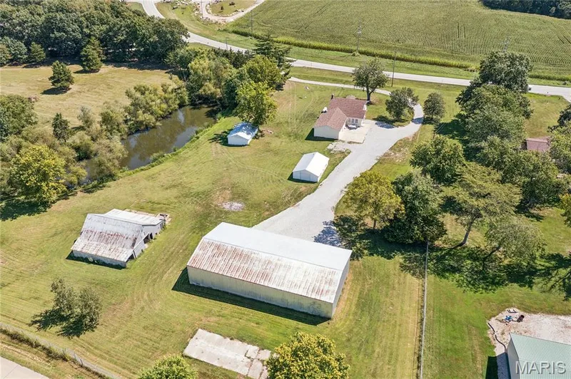 Expansive property featuring a gravel driveway, multiple outbuildings, mature trees, and a natural pond — 435 Highway T, Foristell, MO 63348