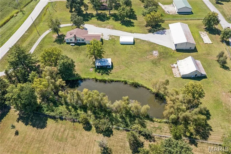 Expansive property featuring a private pond, multiple outbuildings, and a main residence with a red-shingle roof — 435 Highway T, Foristell, MO 63348