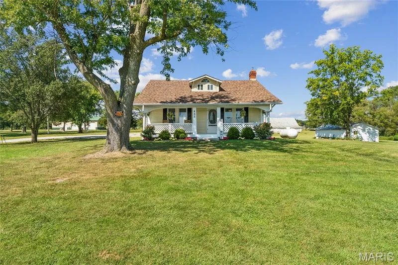 Gable-roof property featuring a covered front porch with white railing, dormer windows, and established trees — 435 Highway T, Foristell, MO 63348