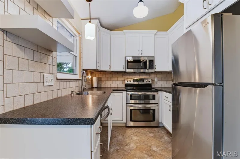 White cabinetry, dark stone-finish countertops, stainless steel appliances, tile backsplash, and tile flooring — 1314 Warrior Song Way, O'Fallon, MO 63366