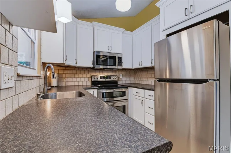 White shaker-style cabinetry with crown molding, stainless steel appliances, dark countertops, and a subway tile backsplash — 1314 Warrior Song Way, O'Fallon, MO 63366