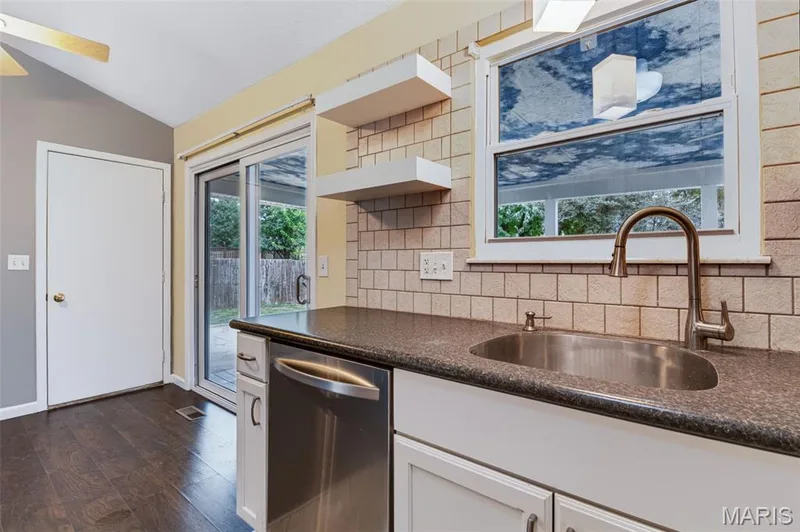 Stainless steel dishwasher, single basin sink with gooseneck faucet, light-colored subway tile backsplash, dark-finish countertops, and white cabinetry — 1314 Warrior Song Way, O'Fallon, MO 63366