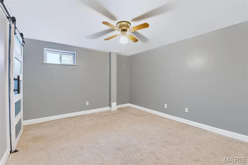 Neutral wall paint, carpet flooring, a ceiling fan with light, and a sliding barn door with frosted panels — 1314 Warrior Song Way, O'Fallon, MO 63366
