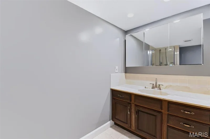 Dark wood-finish vanity with an integrated sink, white countertop, and tile backsplash — 1314 Warrior Song Way, O'Fallon, MO 63366