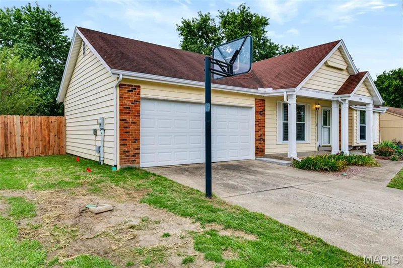 Yellow siding exterior with a two-car garage, brick accents, and a covered entry with columns — 1314 Warrior Song Way, O'Fallon, MO 63366