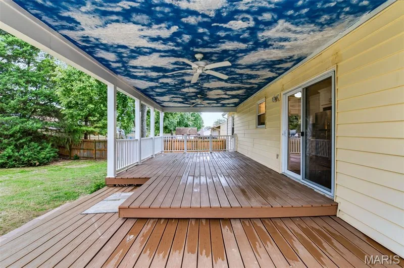 Expansive multi-level wood-finish deck with white railing, covered patio featuring a ceiling fan, and direct access to the interior via a sliding glass door — 1314 Warrior Song Way, O'Fallon, MO 63366
