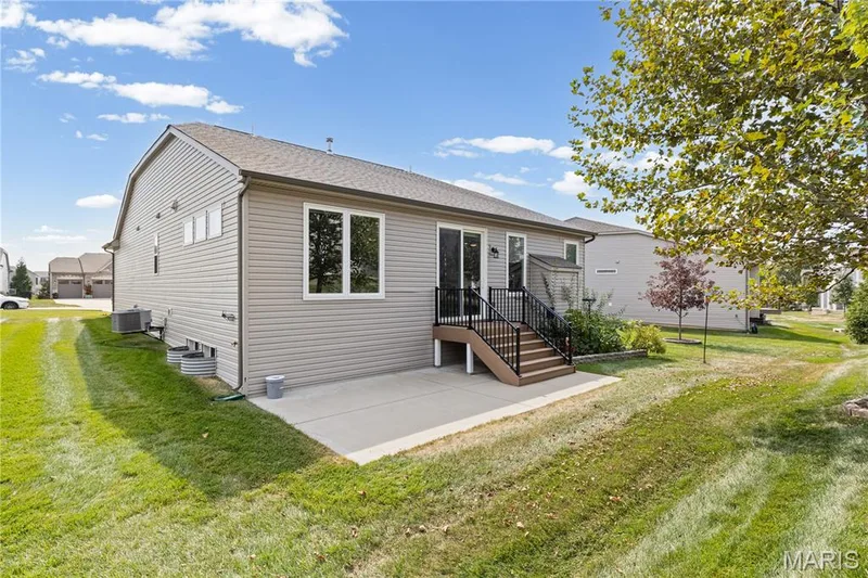 Rear exterior featuring a concrete patio, exterior porch space with dark railings, and sliding glass door access. There is a garden space for those cherished tomatoes, cucumbers or whatever your heart desires. — 89 Alta Mira Court, Dardenne Prairie, MO 63368