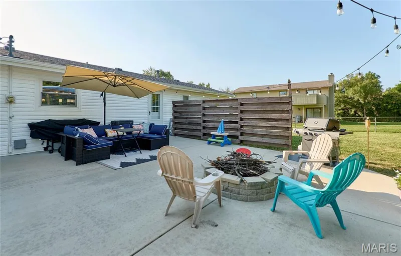Concrete patio featuring a built-in fire pit, string lights, and a wooden privacy fence — 415 Westridge Drive, O'Fallon, MO 63366