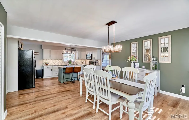 Open-concept floor plan featuring wood-finish flooring, a kitchen island with seating, pendant lighting, and light-toned cabinetry — 415 Westridge Drive, O'Fallon, MO 63366