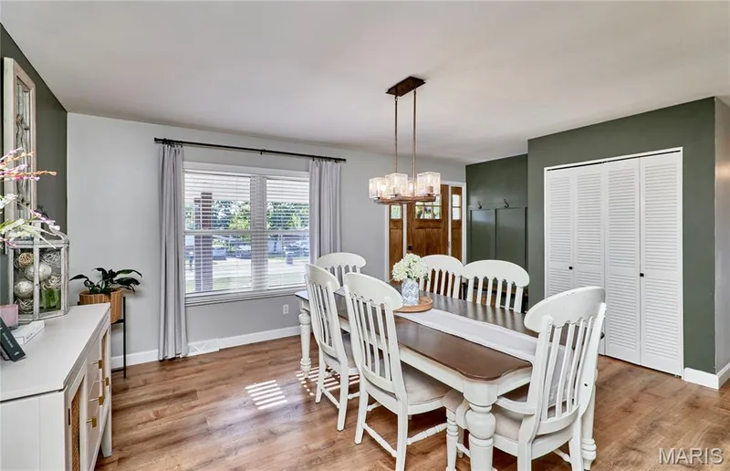 Wood-finish flooring with a multi-paned window featuring blinds, a chandelier with clear glass shades, and white louvered bifold closet doors — 415 Westridge Drive, O'Fallon, MO 63366