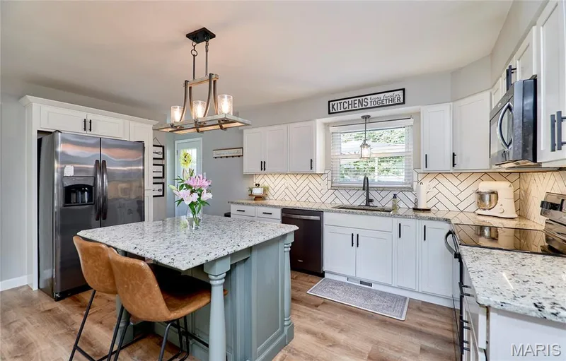 White cabinetry with matte black hardware, stainless steel appliances, herringbone tile backsplash, and wood-finish flooring — 415 Westridge Drive, O'Fallon, MO 63366