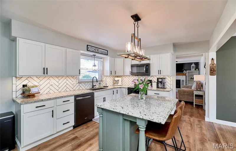 White shaker cabinetry, granite countertops, chevron pattern tile backsplash, wood-finish flooring, and a central island with seating — 415 Westridge Drive, O'Fallon, MO 63366