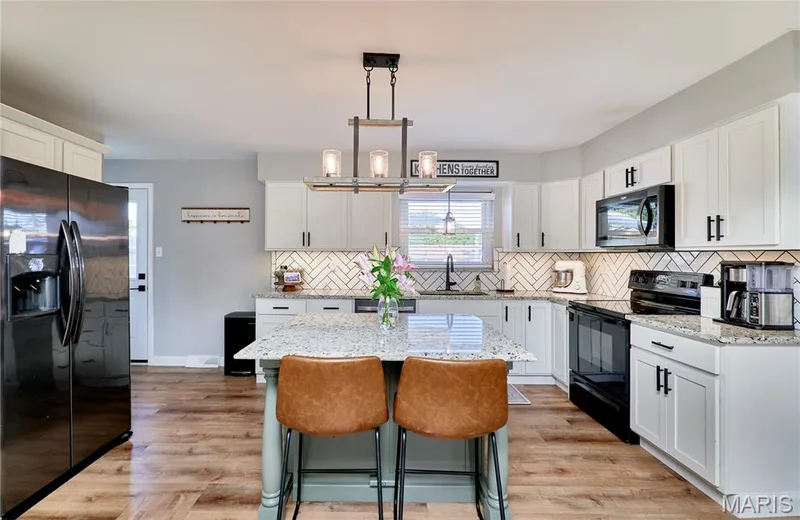 Kitchen featuring light wood-finish flooring, white cabinetry with black hardware, an island with a speckled countertop, black appliances, and a white herringbone tile backsplash — 415 Westridge Drive, O'Fallon, MO 63366
