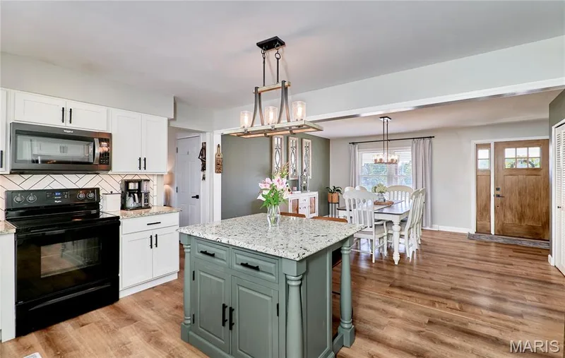 White cabinetry with matte black hardware, black appliances, a herringbone tile backsplash, and a central island with a stone-finish countertop — 415 Westridge Drive, O'Fallon, MO 63366