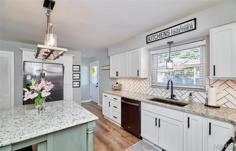 Kitchen featuring white cabinetry, light-colored countertops, a herringbone tile backsplash, wood-finish flooring, and a stainless steel refrigerator — 415 Westridge Drive, O'Fallon, MO 63366