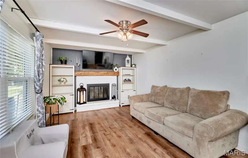 Living area featuring wood-finish flooring, a ceiling fan, exposed ceiling beams, and a fireplace with a wood mantel — 415 Westridge Drive, O'Fallon, MO 63366