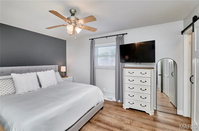 Wood-finish flooring, ceiling fan with integrated lighting, window with blinds, and white barn door entry — 415 Westridge Drive, O'Fallon, MO 63366