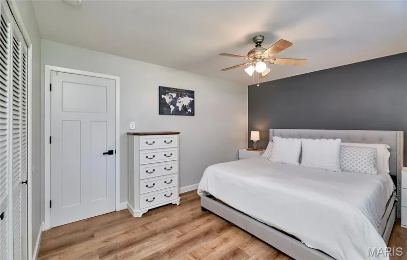 Wood-finish flooring, ceiling fan with integrated lighting, paneled door with matte black hardware, and a louvered bi-fold closet door — 415 Westridge Drive, O'Fallon, MO 63366