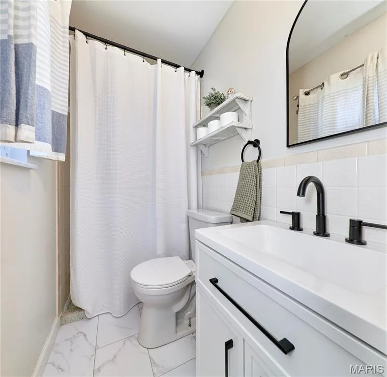 White vanity with black hardware, black faucet, white sink, white tile flooring, and a black-framed mirror — 415 Westridge Drive, O'Fallon, MO 63366