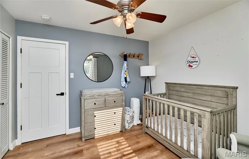Wood-finish flooring, ceiling fan with integrated lighting, paneled door with black hardware, louvered closet door, and two-tone wall finishes — 415 Westridge Drive, O'Fallon, MO 63366