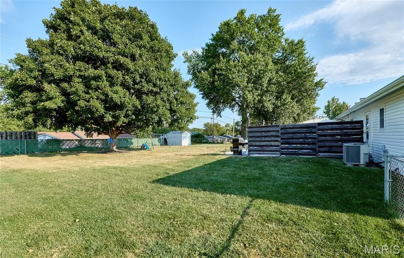 Expansive lawn area, mature trees, wood-finish privacy fence, and a white vinyl siding exterior — 415 Westridge Drive, O'Fallon, MO 63366