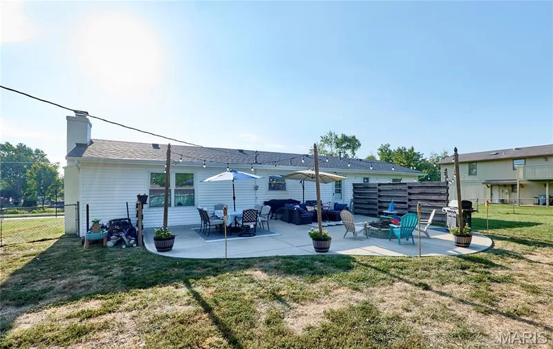 Expansive concrete patio with multiple defined seating areas, string lighting, and a partial wood fence for privacy — 415 Westridge Drive, O'Fallon, MO 63366