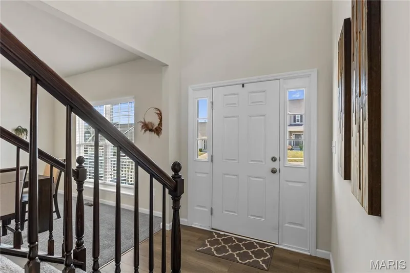 Front door with sidelight windows, wood laminate  flooring, and a dark wood staircase with balusters — 211 Brookview Way Court, O'Fallon, MO 63366