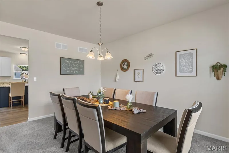 Open-concept dining area with plush grey carpeting, a multi-light chandelier, and light neutral wall tones — 211 Brookview Way Court, O'Fallon, MO 63366