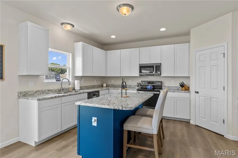 Kitchen featuring a center island, laminate countertops, white cabinetry, stainless steel appliances, and wood laminate flooring — 211 Brookview Way Court, O'Fallon, MO 63366