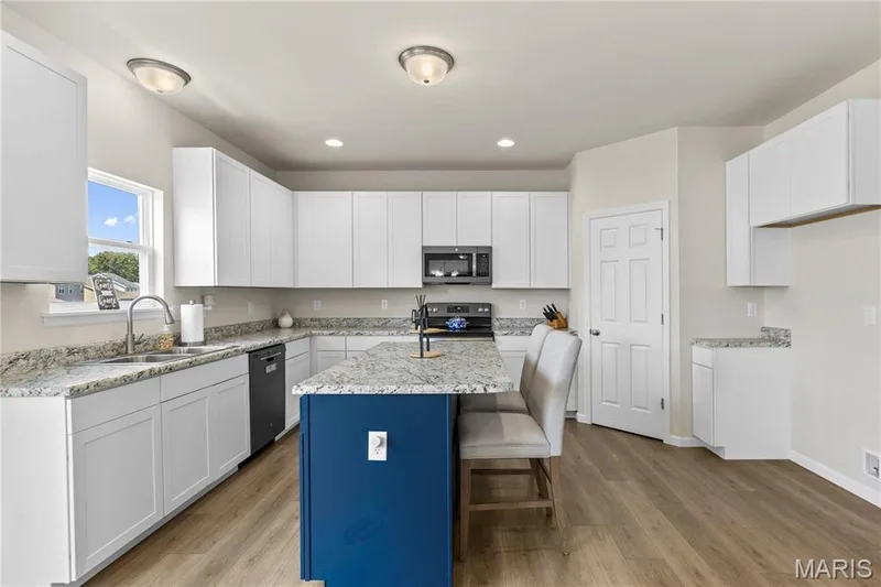 Kitchen featuring an island with seating, white cabinetry, laminate countertops, and wood laminate flooring — 211 Brookview Way Court, O'Fallon, MO 63366