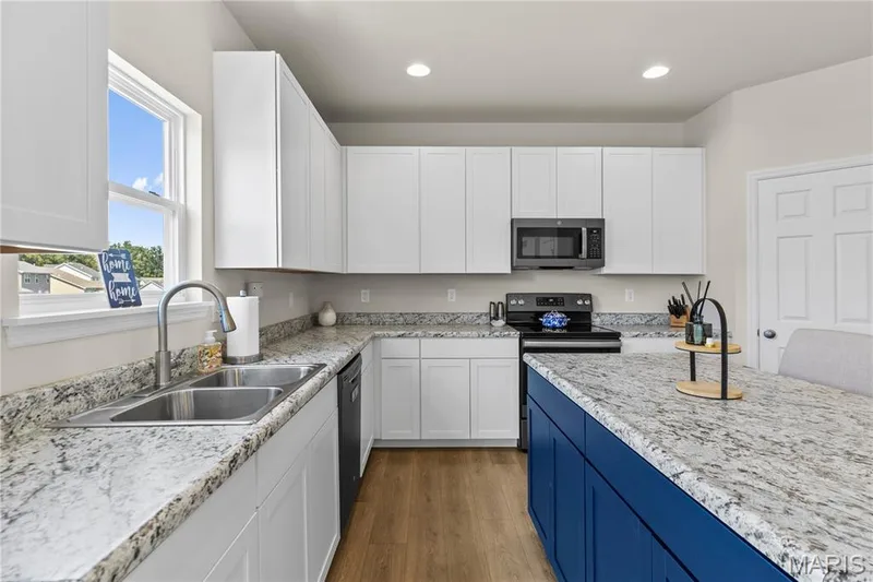 Kitchen featuring stainless steel double basin sink, light-toned wood-laminate flooring, white cabinetry, and a contrasting island with a lighter-toned countertop — 211 Brookview Way Court, O'Fallon, MO 63366