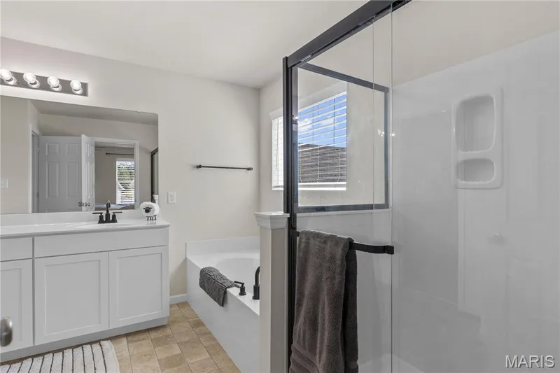 White vanity with a quartz-finish countertop and matte black fixtures, a built-in tub, and a shower with a glass enclosure — 211 Brookview Way Court, O'Fallon, MO 63366