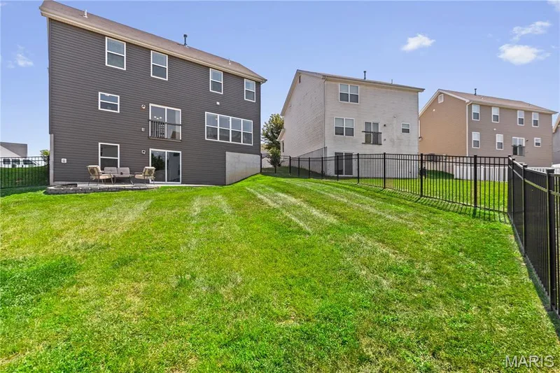 Expansive grassy yard with a black aluminum fence, and a patio featuring a sliding glass door and a 2nd story future deck — 211 Brookview Way Court, O'Fallon, MO 63366