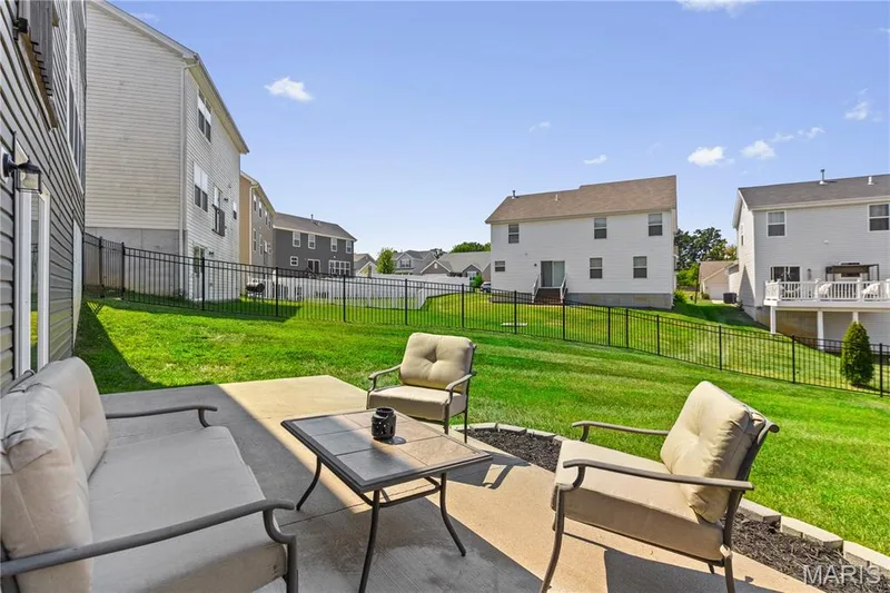 Concrete patio with a black aluminum fence, a grassy yard, and an exterior wall with horizontal siding — 211 Brookview Way Court, O'Fallon, MO 63366