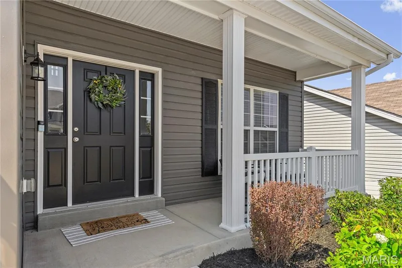 Front entry with black paneled door, sidelight windows, dark siding, and covered porch with white railings and columns — 211 Brookview Way Court, O'Fallon, MO 63366
