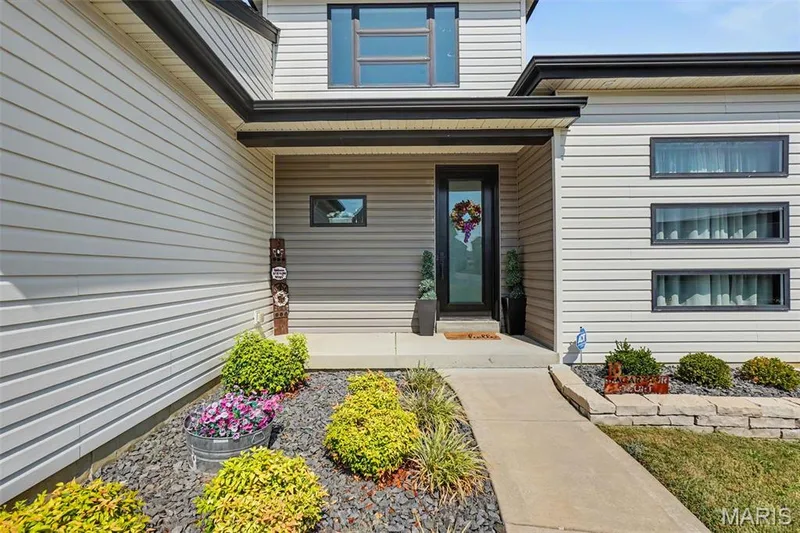 Contemporary façade with horizontal siding, a prominent covered entryway, multiple modern windows, and a stone-edged landscape bed — 18 MacArthur Court, St Charles, MO 63304