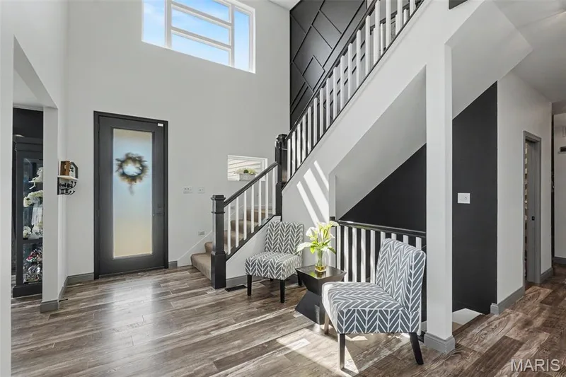 Two-story entryway featuring wood-finish flooring, a contemporary staircase with white balusters, a textured accent wall, and a transom window — 18 MacArthur Court, St Charles, MO 63304