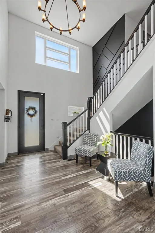 Two-story foyer featuring wood-finish flooring, a contemporary chandelier, a prominent staircase with a custom paneled accent wall, and a large transom window — 18 MacArthur Court, St Charles, MO 63304