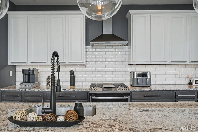 White subway tile backsplash, stainless steel range with hood, white upper cabinetry, dark lower cabinetry, and light-toned countertops — 18 MacArthur Court, St Charles, MO 63304