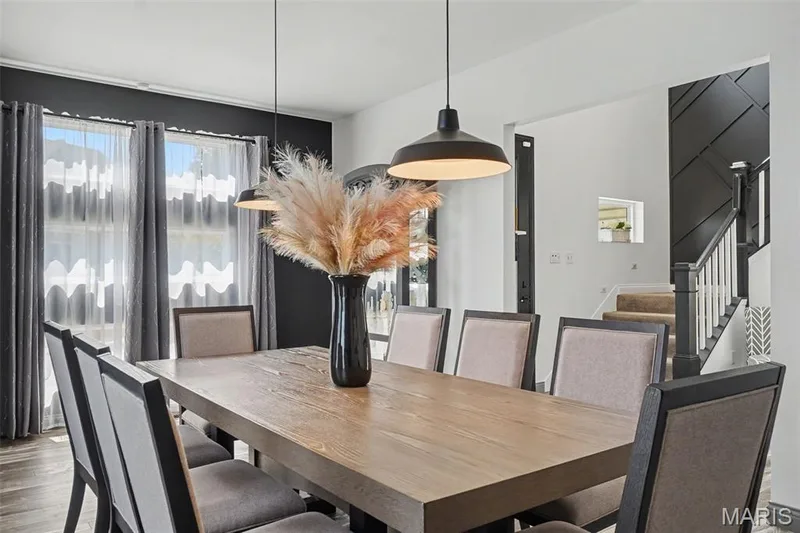 Spacious room featuring a wood-finish dining table, pendant lighting fixtures, and a staircase with a decorative accent wall — 18 MacArthur Court, St Charles, MO 63304