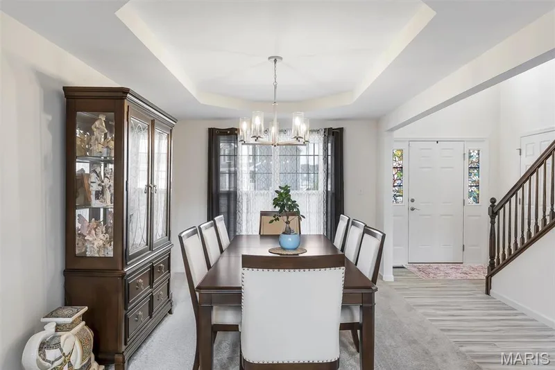 Tray ceiling design with a central chandelier, light-toned wood-finish flooring, and white paneled entry door with decorative glass inserts — 337 White Orchid Court, Wentzville, MO 63385