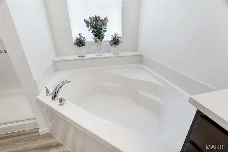 Corner soaking tub with chrome fixtures, integrated shelf, and wood-finish flooring — 337 White Orchid Court, Wentzville, MO 63385