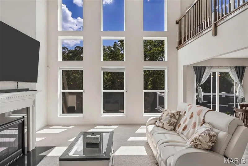 Two-story living area featuring a fireplace with a white mantel, multiple large windows, and an upper-level railing overlooking the space — 337 White Orchid Court, Wentzville, MO 63385