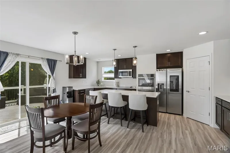 Contemporary kitchen with wood-finish flooring, dark wood cabinetry, stainless steel appliances, a center island with seating, and a sliding glass door leading to an outdoor deck — 337 White Orchid Court, Wentzville, MO 63385