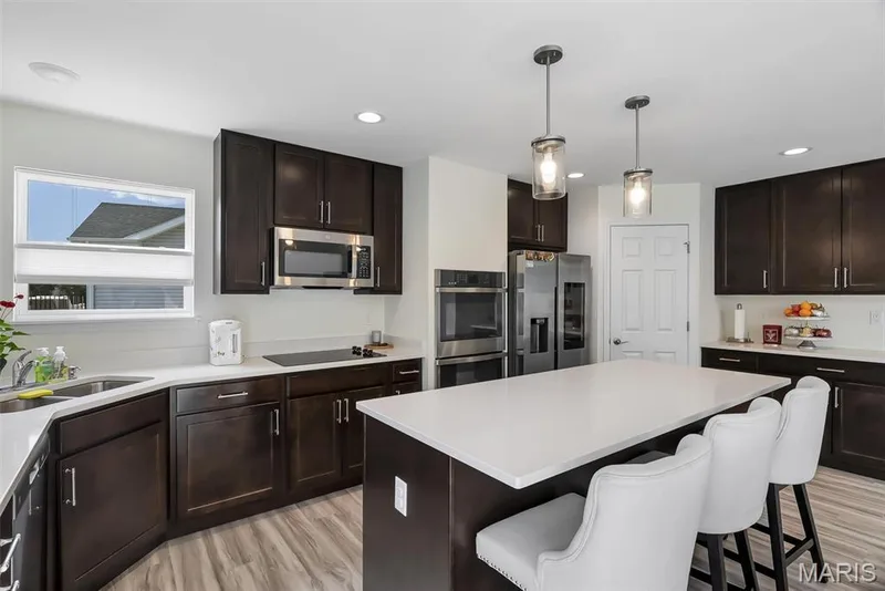 Spacious kitchen with a central island, dark wood-finish cabinetry, light-toned countertops, and stainless steel appliances — 337 White Orchid Court, Wentzville, MO 63385