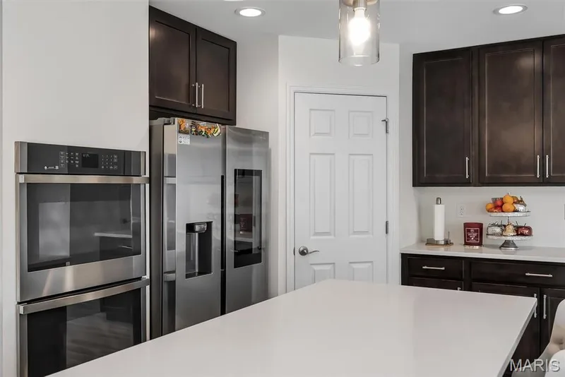 Stainless steel double ovens, stainless steel refrigerator, dark wood-finish cabinetry, white countertop surfaces, and recessed ceiling lighting — 337 White Orchid Court, Wentzville, MO 63385