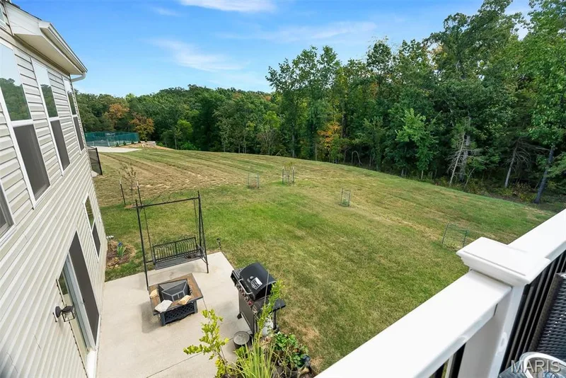 Expansive exterior featuring a concrete patio, verdant lawn, and wooded backdrop — 337 White Orchid Court, Wentzville, MO 63385